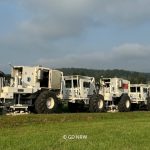 Kolonne von Vibro-Trucks auf grüner Wiese mit leicht bewölktem Himmel.