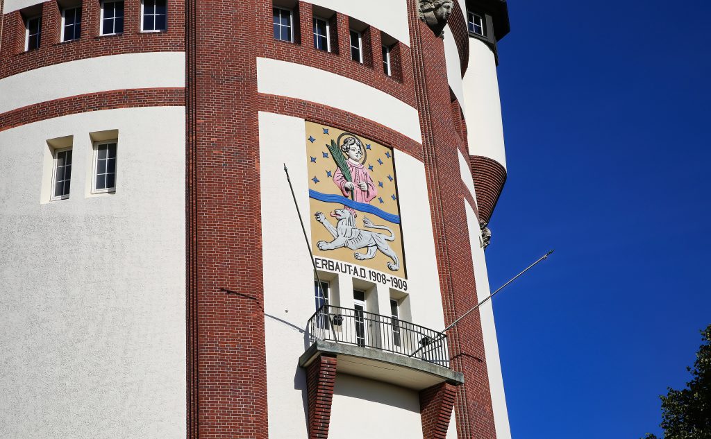 Wasserturm Mönchengladbach, sichbar ist ein Teil der Fassade mit dem Wappen Engel und Löwe vor blauem Himmel