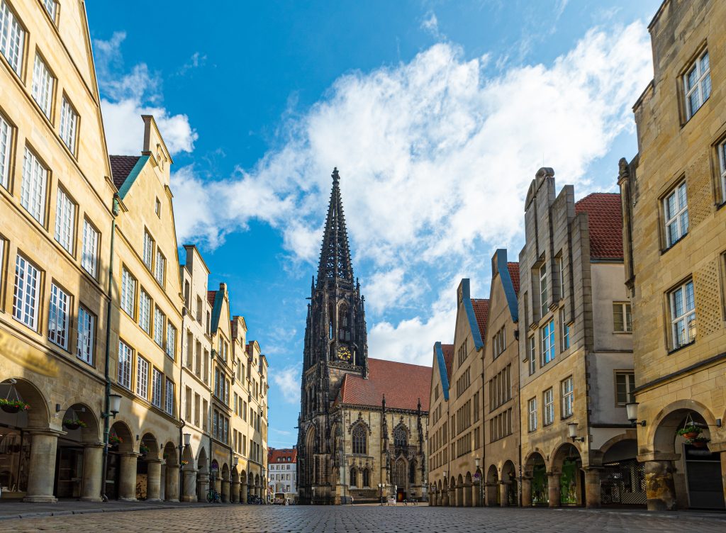 Prinzipalmarkt in Münster, Hausfassaden und im Hintergrund die Lambertikirche, blauer Himmel mit Schäfchenwolken